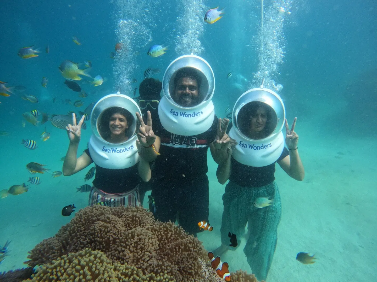 Tourists wearing sea-walk helmets walking on the ocean floor and feeding colorful tropical fish in Andaman