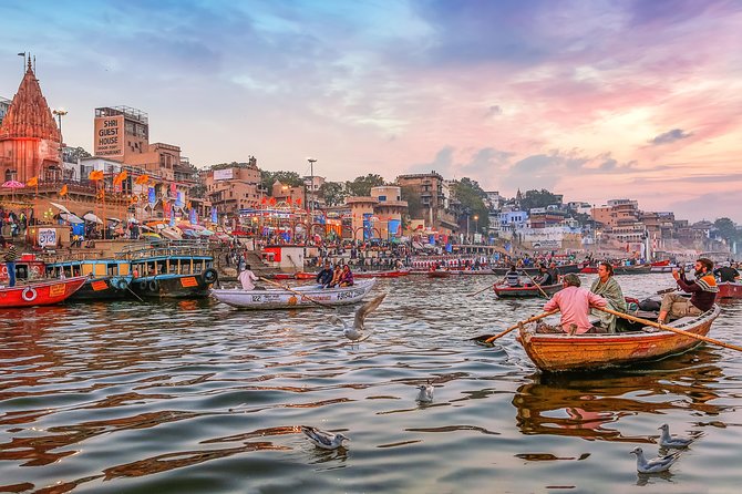 A wooden rowboat gently floating on the Ganges river at sunrise with ancient Varanasi ghats in the background